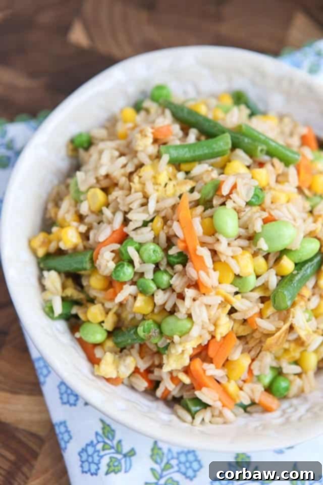 A close-up shot of steaming 5-ingredient vegetable fried brown rice, showcasing a medley of colorful vegetables and scrambled egg pieces, served in a white bowl.