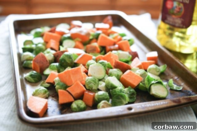 Sheet pan with uncooked cubed sweet potatoes and halved Brussels sprouts, ready for roasting.