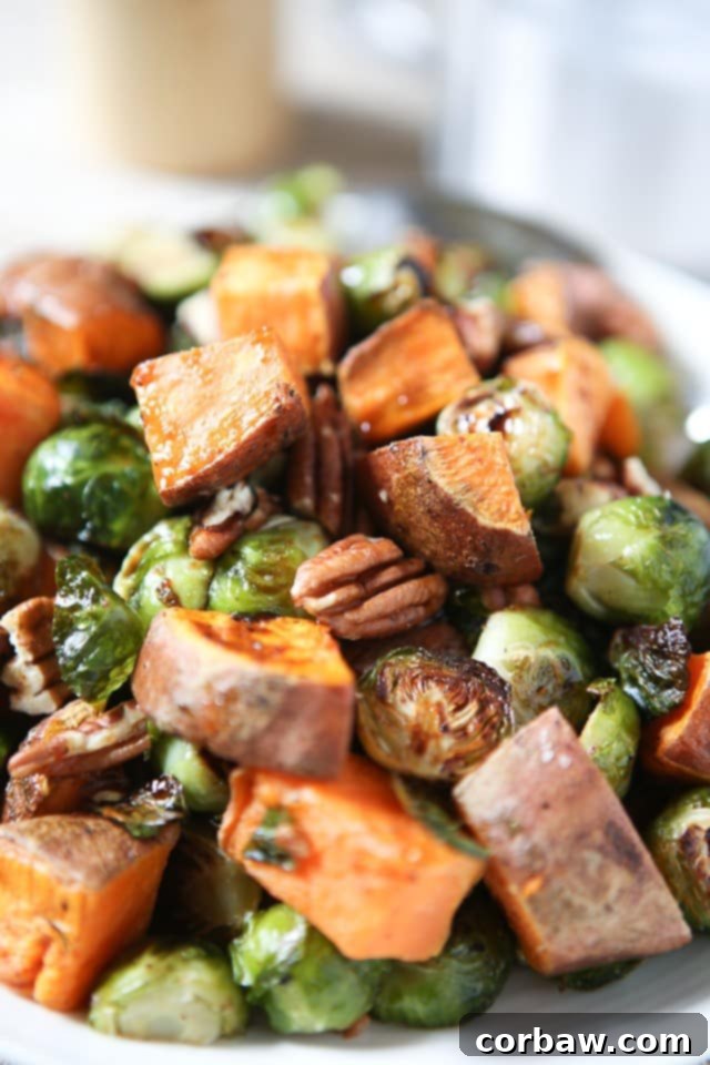 A vibrant close-up shot of roasted sweet potatoes, Brussels sprouts, and crunchy pecans, glistening with a maple, balsamic, and sriracha glaze. An ideal holiday side dish to #ThinkFisher about!