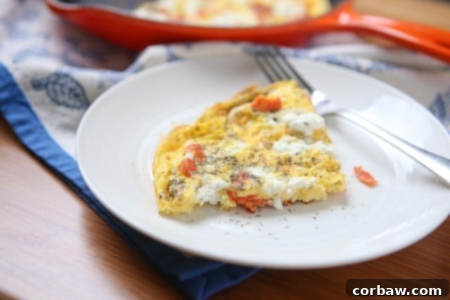 Plate of Smoked Salmon Frittata A slice of cooked smoked salmon frittata with goat cheese and dill, served on a white plate, showcasing its fluffy texture and colorful ingredients.