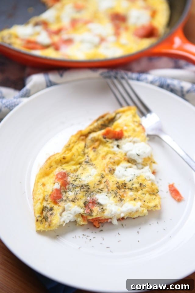 Smoked Salmon Frittata Close-up A delicious smoked salmon frittata loaded with goat cheese and fresh dill, freshly cooked in a cast-iron skillet, showcasing its vibrant ingredients.