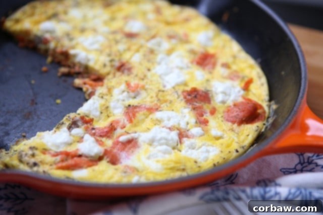 Skillet Smoked Salmon Frittata A freshly cooked smoked salmon frittata in a cast-iron skillet, topped with crumbled goat cheese and dill, ready for serving.
