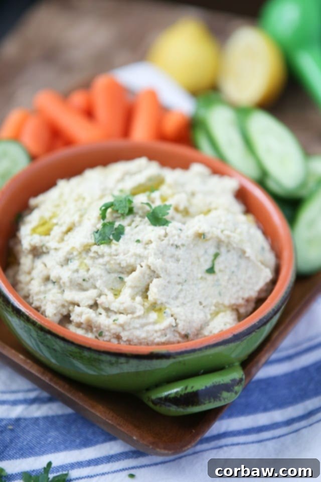 A vibrant bowl of Lemony Artichoke Hummus, garnished with fresh parsley and a drizzle of olive oil, surrounded by crisp pita chips and fresh vegetables like cucumber and carrots, perfect for a healthy snack or appetizer.
