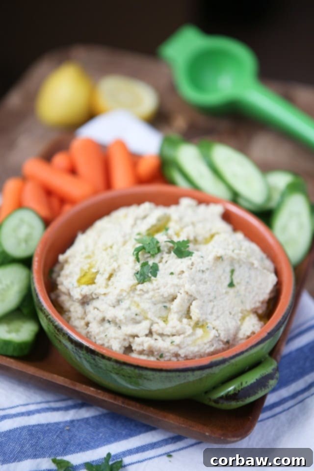 A serving of Lemony Artichoke Hummus in a rustic bowl, with a spoon nestled in it, surrounded by fresh lemons and parsley, emphasizing its homemade goodness.