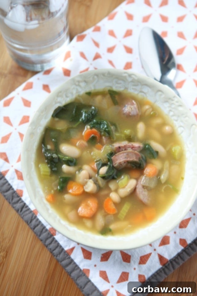 It's definitely soup season and one of my family's favorite soups is this Smoked Sausage and White Bean Soup with Spinach. It will warm you right up! #soup #healthyrecipe #healthysoup A close-up shot of the steaming Smoked Sausage and White Bean Soup with Spinach, ready to be served in a rustic bowl.