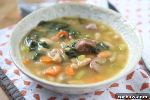It's definitely soup season and one of my family's favorite soups is this Smoked Sausage and White Bean Soup with Spinach. It will warm you right up! An overhead view of the Smoked Sausage and White Bean Soup with Spinach, garnished lightly and ready to be enjoyed.