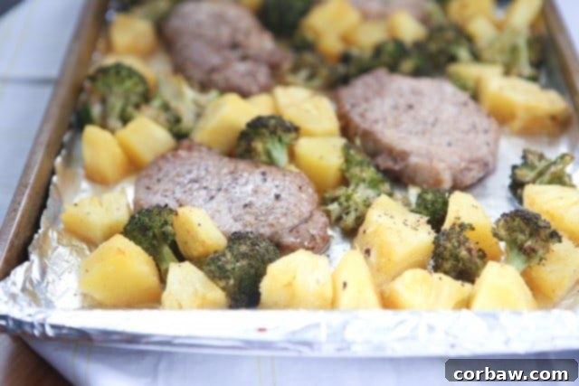 Close-up shot of the finished Chinese Five Spice Sheet Pan Pork Chops with tender roasted broccoli and caramelized pineapple, garnished with sesame seeds. A wholesome, quick, and flavorful family dinner.