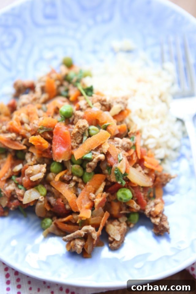 Healthy Kheema: Spiced Ground Turkey and Peas A vibrant plate of Kheema, featuring spiced ground turkey, carrots, peas, and onions, served over fluffy rice, garnished with fresh cilantro.