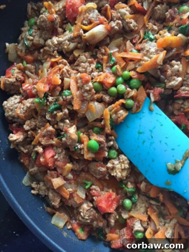 Kheema Skillet: Ground Turkey and Spices A skillet full of cooked Kheema, featuring spiced ground turkey, tender carrots, bright green peas, and finely chopped onions, with a blue spatula resting inside.