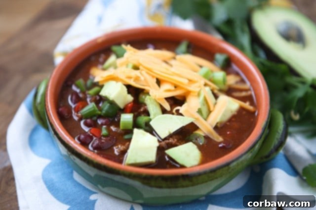 Chipotle Chicken Chili bowl of chili topped with shredded cheese, diced avocado, and scallions