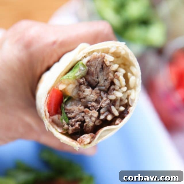hand holding a wrapped turkey and black bean burrito with a bite, showing the fillings