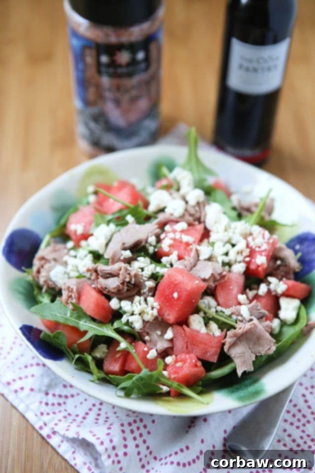 Vibrant summer salad with fresh spinach, arugula, sweet watermelon chunks, and savory roast beef slices, perfect for a light lunch.