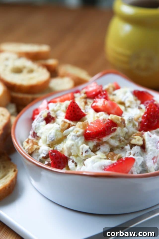 A vibrant bowl filled with creamy goat cheese spread, fresh strawberries, aromatic basil, and crunchy walnuts, ready to be served.