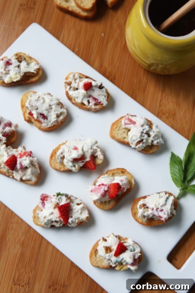 A white platter showcasing several perfectly topped snack toasts with creamy goat cheese and strawberry spread, garnished with basil.