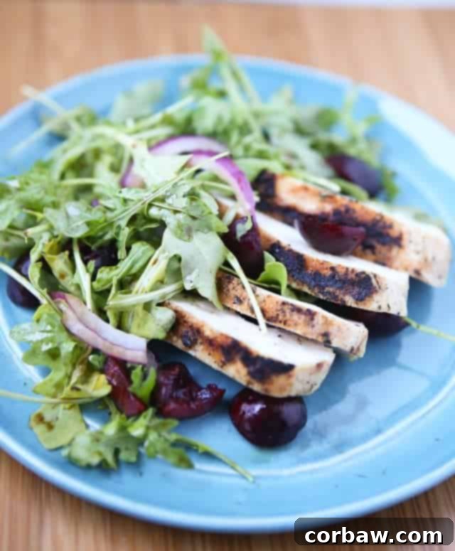 A beautifully arranged plate featuring tender grilled chicken slices, vibrant red cherries, and thinly sliced red onions, all served on a bed of fresh, peppery arugula. It's a perfect visual representation of a light, low-carb, and flavorful summer meal.