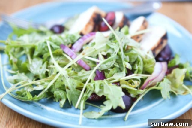 A close-up view of the grilled chicken with cherry arugula salad, showcasing the beautifully charred chicken slices, glistening halved cherries, and thinly sliced red onions nestled on a vibrant bed of fresh arugula, ready to be enjoyed.