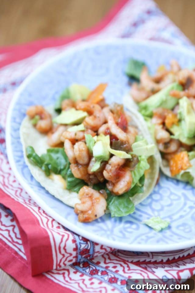 A vibrant plate featuring two corn tortillas generously stuffed with perfectly cooked shrimp, crisp romaine lettuce, and creamy avocado slices, all drizzled with a colorful mango salsa, ready to be enjoyed.