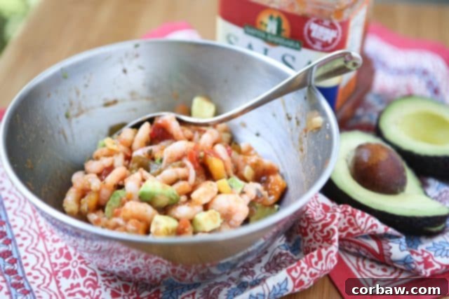 A beautifully arranged bowl of seasoned shrimp mixture sits on a rustic tapestry, accompanied by a perfectly sliced avocado and a separate bowl of vibrant mango salsa, highlighting the fresh ingredients for the tacos.