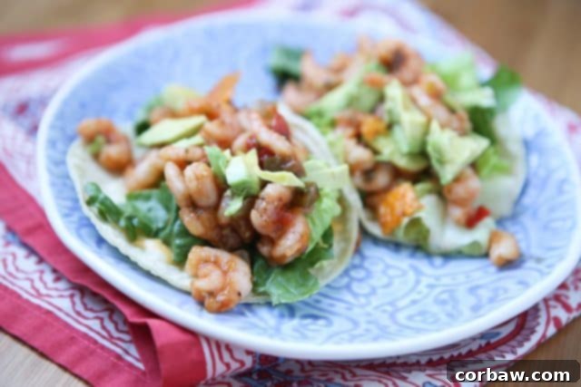 Two fully assembled shrimp tacos presented on a white plate, showcasing the vibrant fillings of seasoned shrimp, crisp lettuce, creamy avocado slices, and colorful mango salsa, ready for a delightful meal.