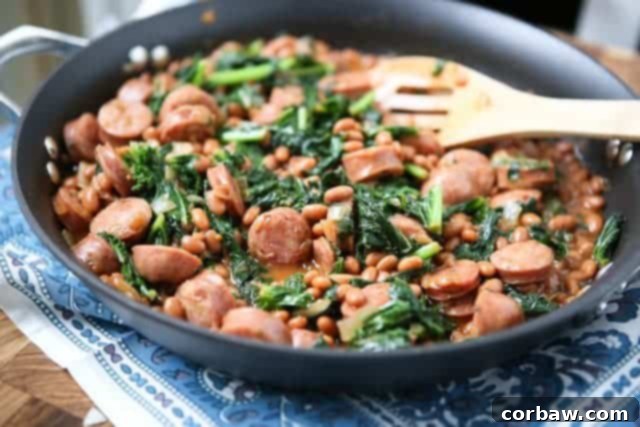 Close-up of a rustic skillet filled with smoky chicken sausage, robust baked beans, and nutrient-rich wilted kale, accompanied by a wooden serving spoon.