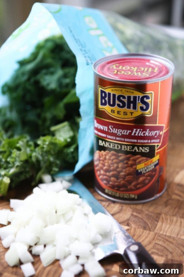 Ingredients for Baked Bean, Sausage, and Kale Skillet: A can of Bush's Brown Sugar Hickory Baked Beans, a bunch of fresh kale, and expertly chopped white onions on a wooden cutting board with a sharp knife.