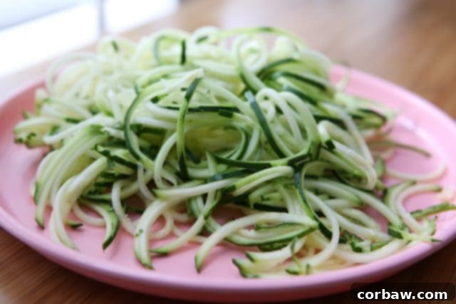 Fresh Zoodles: The Healthy Base Freshly spiralized zucchini noodles (zoodles) ready for cooking on a plate, showcasing their vibrant green color.