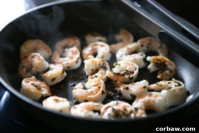 Shrimp Sautéing in a Skillet Succulent shrimp cooking in a nonstick skillet, seasoned with herbs and spices, ready to be incorporated into the zoodle dish.