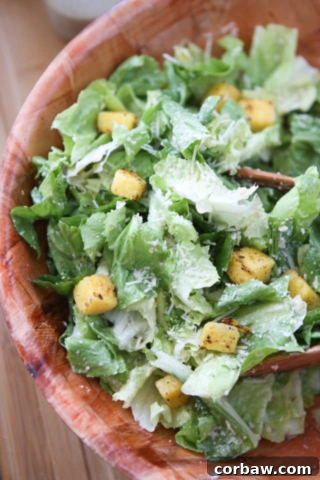 Large wooden bowl filled with vibrant Escarole Caesar Salad, generously topped with golden Polenta Croutons and drizzled with a rich Parmesan Walnut Lemon Vinaigrette. A perfect healthy holiday salad that's a fresh twist on a classic.