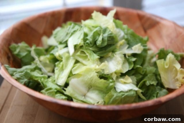 Large wooden bowl filled with freshly chopped romaine lettuce, ready to be combined with escarole for a unique Caesar salad base.