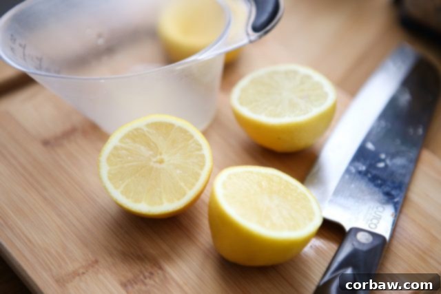 Two vibrant yellow lemons, freshly sliced in half, resting on a rustic wooden cutting board alongside a measuring cup and a large chef's knife. This highlights the essential, bright citrus component for the Parmesan Walnut Lemon Vinaigrette.
