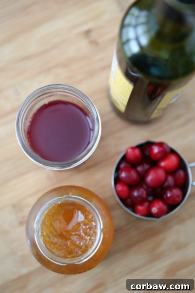 jar of orange marmalade, container of cranberries, and cup of cranberry juice sitting next to its container on a wooden countertop