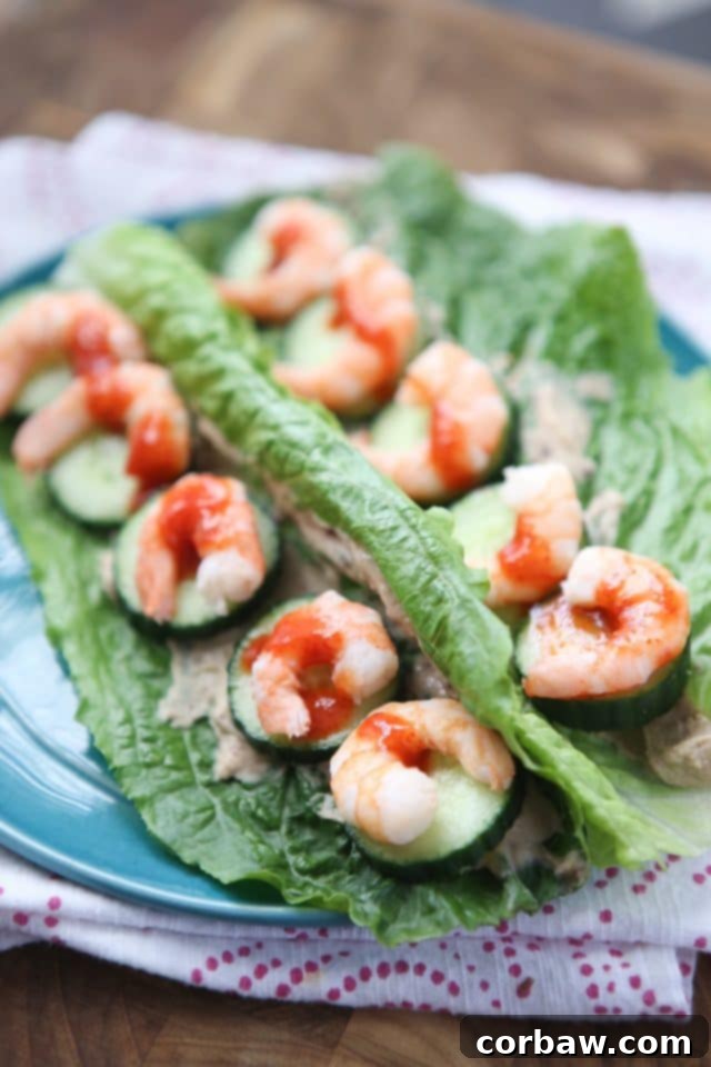 Sriracha Shrimp and Hummus Lettuce Wraps plate of 2 romaine lettuce leaves stuffed with shrimp and cucumber, drizzled with hot sauce