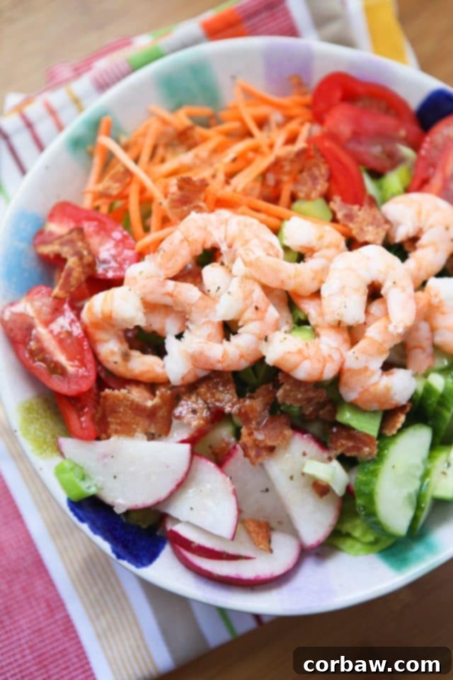 A vibrant bowl of fresh garden salad with succulent cooked shrimp, crispy bacon crumbles, shredded carrots, juicy grape tomatoes, refreshing cucumber slices, and crisp radishes, all arranged beautifully for a healthy and appealing meal.