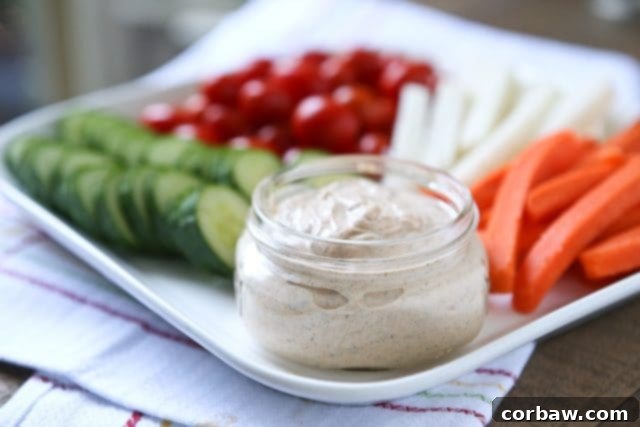 Close-up of the creamy Chipotle Ranch Greek Yogurt Dip with a hand dipping a carrot stick.