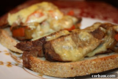 Two open-faced Guinness braised brisket sandwiches on toasted rye bread with beautifully melted Kerrygold Swiss cheese, served alongside a small bowl of rich Guinness gravy for dipping.