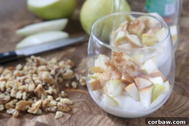 Stacked layers of Greek yogurt, spiced pears, and chopped walnuts in a glass, ready to be enjoyed as a healthy and flavorful fall dessert or snack. A beautiful visual of the parfait ingredients.