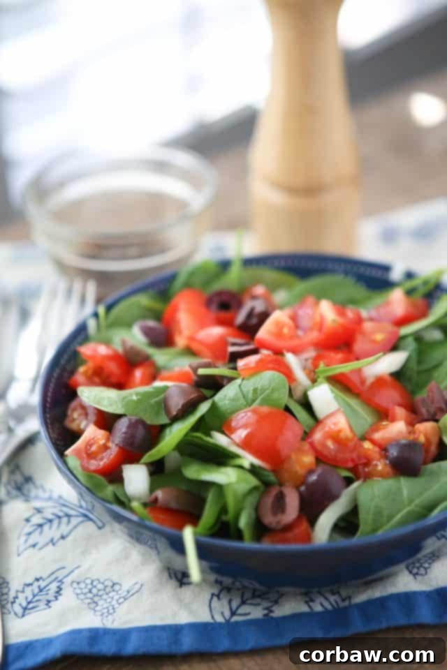 A close-up of a colorful chopped tomato and spinach salad with Kalamata olives and red onion, dressed lightly with vinaigrette, perfect for an easy, healthy summer meal.