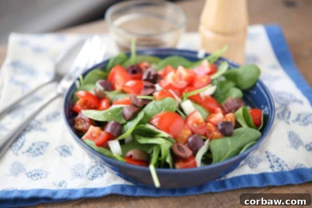Close up image of chopped tomatoes, spinach leaves, and red onions with Kalamata olives in a bowl, ready for a light dressing.