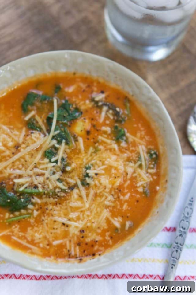 An inviting overhead shot of a bowl of Tomato and Spinach Tortellini Soup, accompanied by a glass of water, emphasizing a simple and satisfying meal.