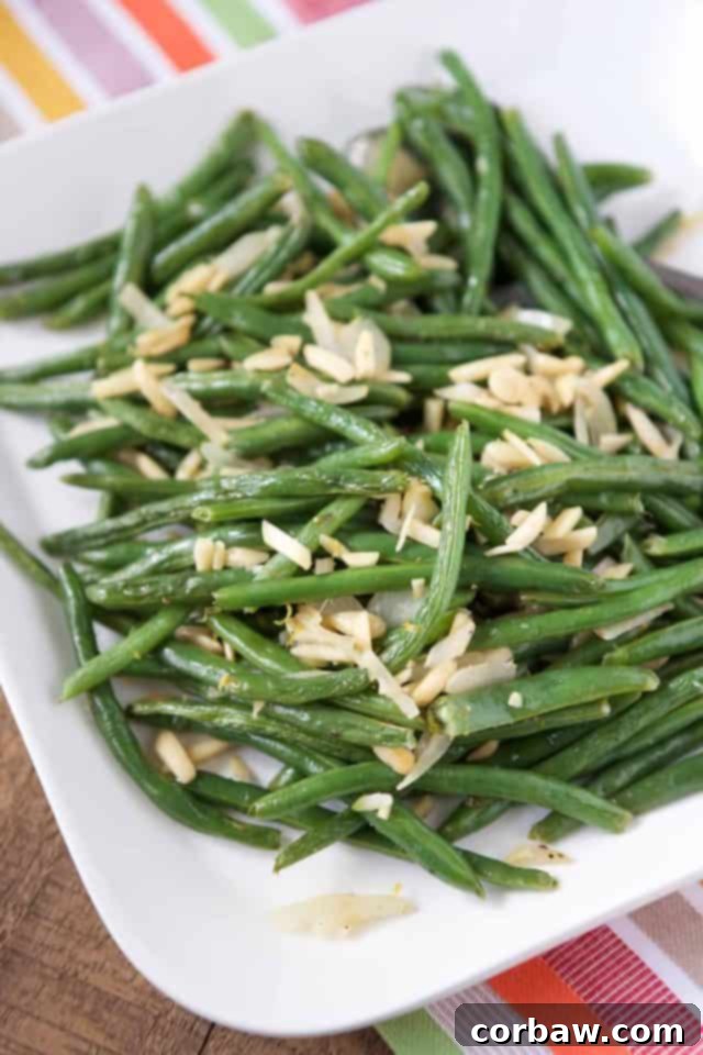 A white platter generously filled with perfectly roasted green beans and toasted almonds, ready to serve.