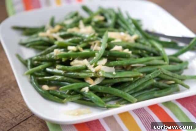 Close-up of vibrant green beans topped with golden brown almonds and lemon zest on a white serving platter.