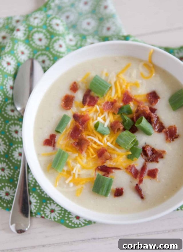 overhead shot of white bowl filled with creamy cauliflower potato soup topped with cheese, green onion and bacon
