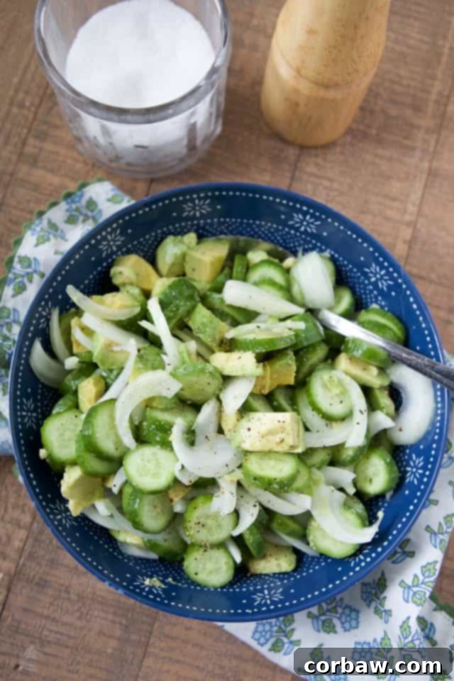 Bright green sliced cucumbers, red onion, and creamy diced avocado in a vibrant blue bowl, perfectly tossed with fresh lemon, sea salt, and black pepper, ready to serve as a refreshing summer side dish.