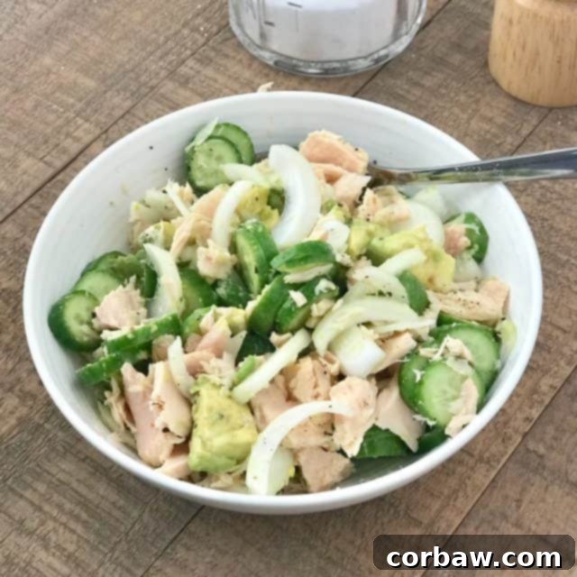 A refreshing cucumber, avocado, and onion salad served in a white bowl, explicitly featuring flaked tuna as a high-protein addition, making it a complete and healthy meal, ready in minutes.
