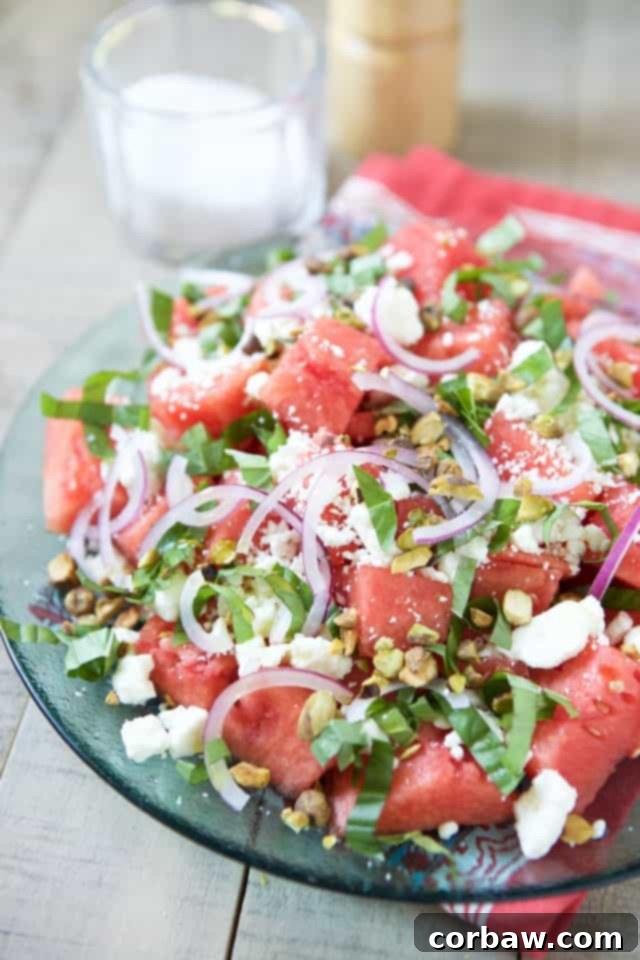 Overhead shot of a beautifully arranged Watermelon Feta Salad with vibrant red watermelon, white feta crumbles, green basil, and chopped pistachios in a shallow white bowl.