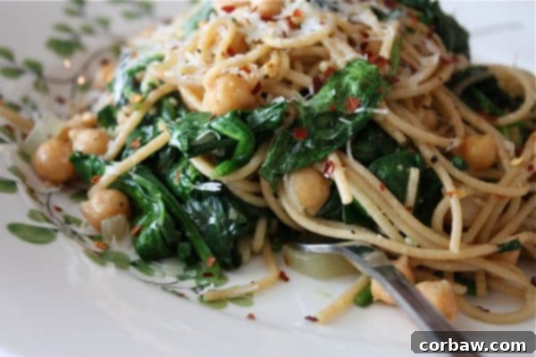 Close-up of Whole Wheat Spaghetti with Chickpeas and Spinach, garnished with fresh Parmesan and red pepper flakes.