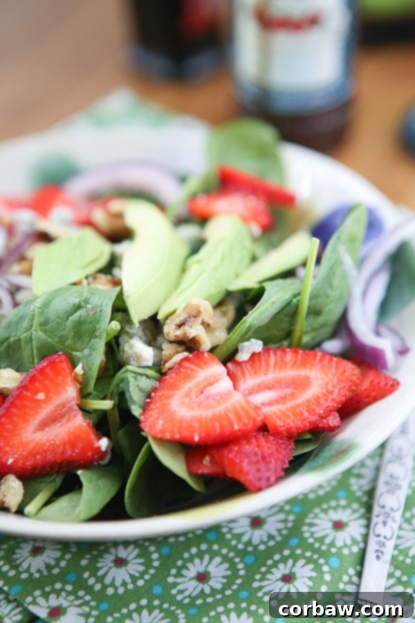 Strawberry Spinach and Walnut Salad with Raspberry Balsamic Vinaigrette A hearty bowl of spinach salad generously topped with fresh strawberry slices, creamy avocado, and crunchy walnuts, ready to be dressed.