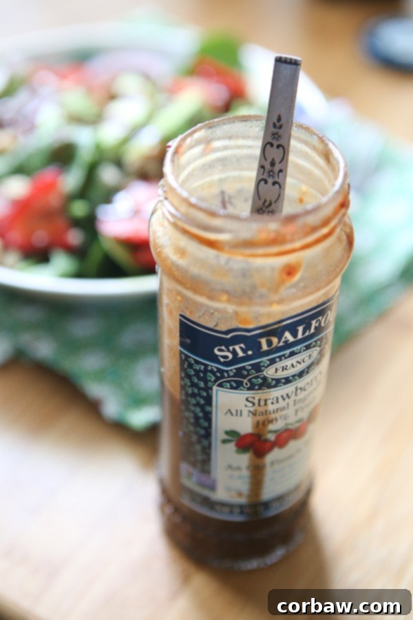Strawberry Spinach and Walnut Salad with Raspberry Balsamic Vinaigrette An open glass jar of strawberry preserves with a spoon inside, showcasing the last delicious spoonfuls.
