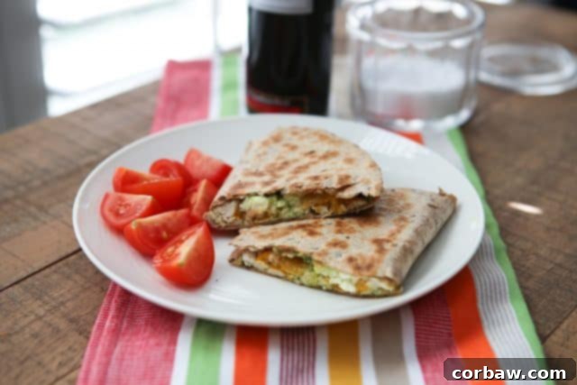 A Pesto Chicken Quesadilla expertly cut in half, revealing a generous and colorful filling of chicken, bright green pesto, melted cheese, and roasted red peppers, served hot and inviting.