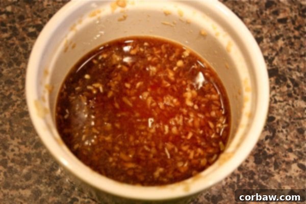 A small glass bowl filled with the homemade stir-fry sauce ingredients: soy sauce, rice vinegar, freshly grated ginger, and minced garlic, ready to be added to the healthy salmon and veggie dinner.